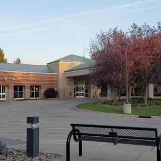 A building entrance with a bench and autumn trees in the foreground.