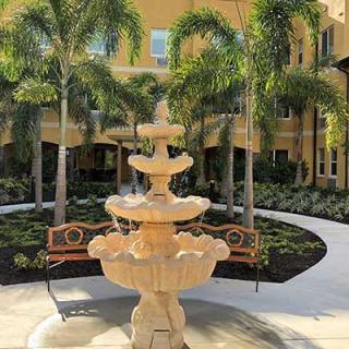 A beautiful courtyard with a three-tiered fountain surrounded by palm trees and lush greenery.