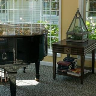 A sunlit living room featuring a grand piano and a side table with books.
