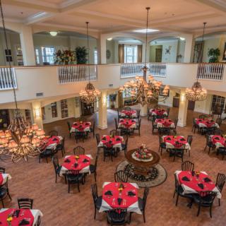 A spacious and elegant dining area featuring multiple tables with red tablecloths, ornate chandeliers, and a classic interior design.