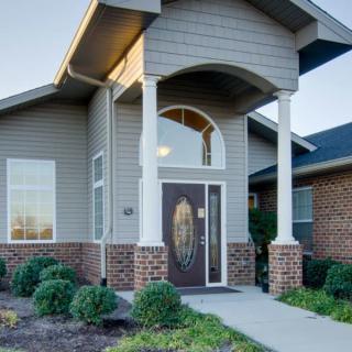 A modern house entrance featuring brick siding, columns, and well-maintained landscaping.