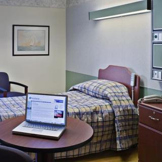 A hospital room with a single bed, a table, and a laptop.