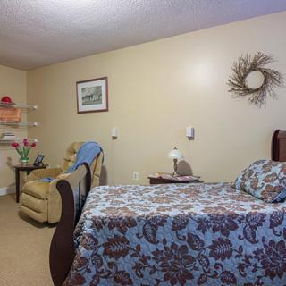 A cozy bedroom interior with a bed, chair, and decorative elements.