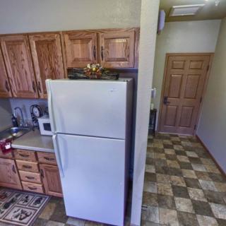 A small kitchen with wooden cabinets, a white refrigerator, and a microwave, leading into a tiled hallway.