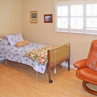 A cozy bedroom with a single bed, an orange armchair, and light wooden flooring.
