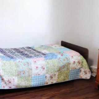 A minimalist bedroom with a single bed featuring a colorful quilt on a wooden floor.