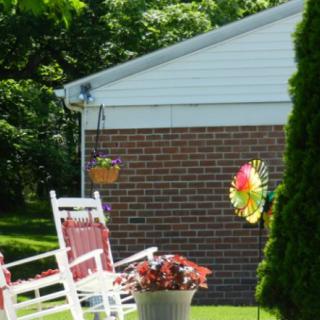 A peaceful garden scene with rocking chairs, a colorful wind spinner, and vibrant flowers.