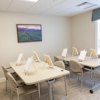 A well-lit classroom with tables and chairs arranged neatly, equipped with easels for painting activities.