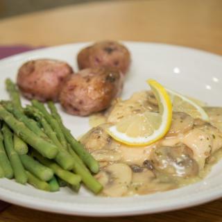 A plate of chicken with a creamy sauce, served with asparagus and red potatoes.
