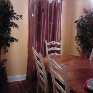 A cozy dining room with a wooden table and chairs, accented by curtains and decorative plants.