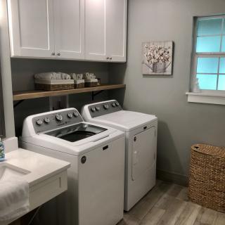 A neatly organized laundry room with a washing machine and dryer, featuring cabinets, a shelf, and a basket.