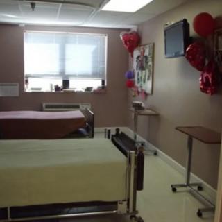 A hospital room with two beds, balloons, and a television.