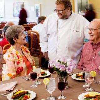 A chef interacting with senior diners at a restaurant table.