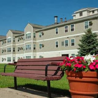 A serene view of an apartment building with a bench and colorful flowers in the foreground.