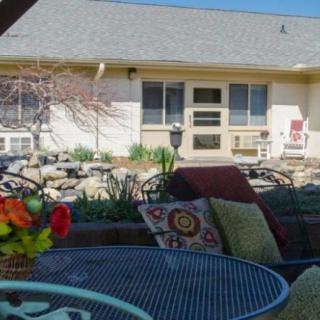 A cozy outdoor patio area with a table set and cushions, overlooking a garden in front of a building.
