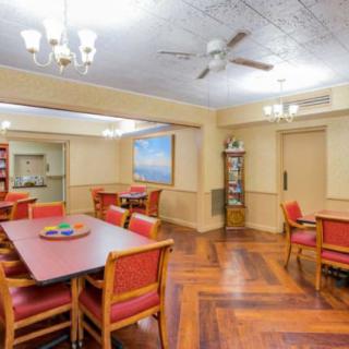 A cozy dining room with wooden floors, red cushioned chairs, and elegant lighting fixtures.