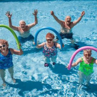 A group of seniors enjoying water aerobics in a swimming pool with colorful noodles.