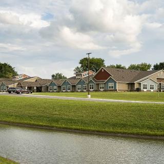 A picturesque residential area with houses and a pond under a partly cloudy sky.