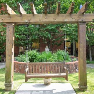 A charming garden swing under a wooden pergola, surrounded by lush greenery.