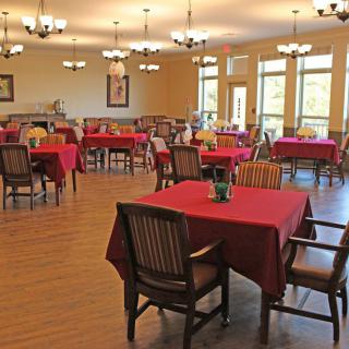 A spacious dining room with red tablecloths, wooden chairs, and chandeliers.