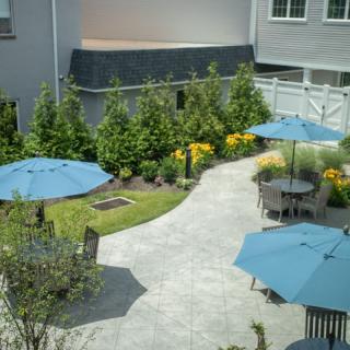 A well-manicured garden patio with tables and blue umbrellas providing shade along a winding pathway.