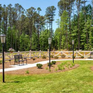 A scenic garden area with benches, lamp posts, and a winding pathway surrounded by trees.