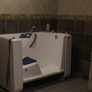 An accessible bathroom featuring a walk-in tub with tiled walls.