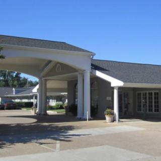 A building entrance with a covered driveway and columns, set against a clear blue sky.