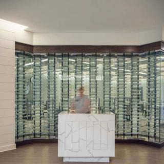 A modern office reception area with a sleek glass wall backdrop and a central white reception desk.