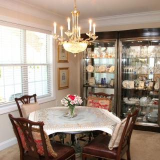 A cozy dining room with a chandelier, showcasing a table set for four and a cabinet filled with decorative items.