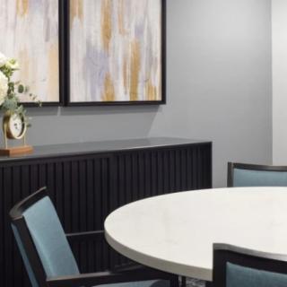 A modern conference room featuring a round table, chairs, abstract artwork, and decorative flowers.