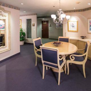 A cozy dining area with a round table and classic chairs, adorned with a chandelier, artwork, and a large mirror on the wall.