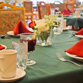 A neatly set dining table with red napkins, glasses, and a floral centerpiece.