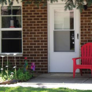 A brick house entrance with a red chair and small garden.