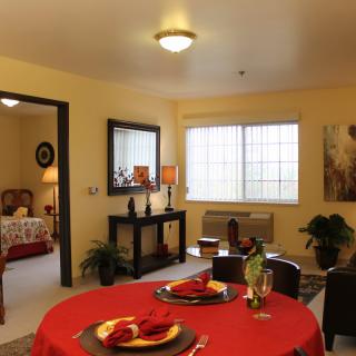 A cozy living and dining area with warm lighting, featuring a red tablecloth, decorative plants, and stylish home decor.