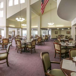 An empty dining room with neatly arranged tables and chairs, featuring chandeliers and carpet flooring.
