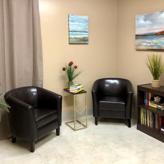 A cozy office corner with two black chairs, a small side table with decorative items, and wall art.
