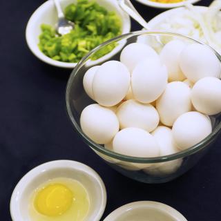 A bowl of eggs surrounded by various cooking ingredients ready for preparation.