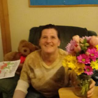 A woman smiles happily while holding a bouquet of vibrant flowers in a cozy indoor setting.