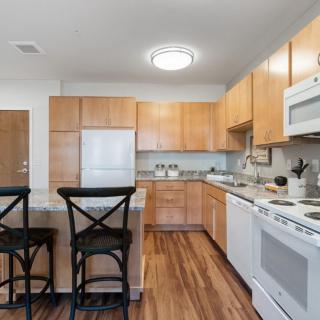 A modern kitchen with wooden cabinets, white appliances, and counter stools.