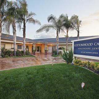 A building entrance surrounded by palm trees and a well-maintained lawn, with a visible sign on the right.