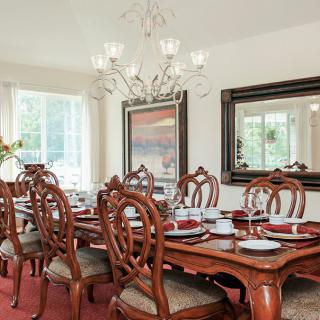 An elegant dining room featuring a large wooden table set with dishes and surrounded by ornate chairs, illuminated by a modern chandelier.