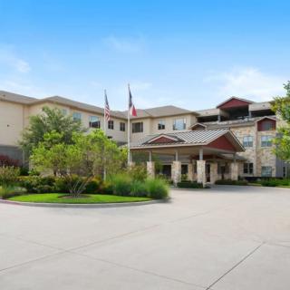 A view of a hotel building with a circular driveway and surrounding greenery.