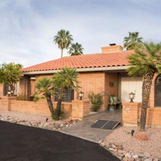 A single-story house with a brick exterior and palm trees in a desert landscape.