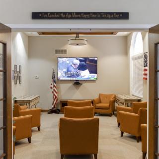 A well-furnished waiting room with leather chairs, a television on the wall, and an American flag.