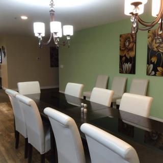 A modern dining room with a long table, surrounded by upholstered chairs and illuminated by elegant chandeliers.