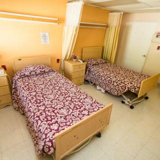 A shared patient room in a hospital featuring two beds with patterned bedding and orange walls.