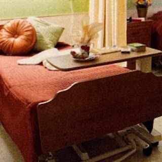 A cozy hospital room featuring a neatly made bed with colorful pillows and a bedside table.