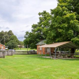 A spacious yard with a grassy area, several trees, a small brick building, and a covered outdoor shelter.