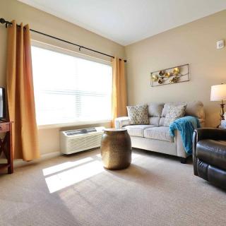 A cozy living room with a sofa, armchair, and large window letting in natural light.